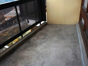 Ein Balkon mit Betonboden, einem schwarzen Metallgeländer und einer beige farbenen Wand.