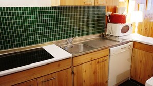 Una cocina con armarios de madera, salpicadero de azulejos verdes, un lavabo, un microondas y un lavavajillas.
