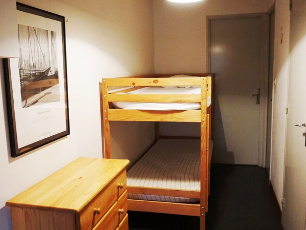 A small, narrow room with a bunk bed, a wooden dresser, and a framed picture on the wall.