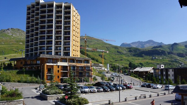Un hotel de varios pisos con diseño moderno, situado en una zona montañosa, con estacionamiento y señalización de un centro de esquí cerca.
