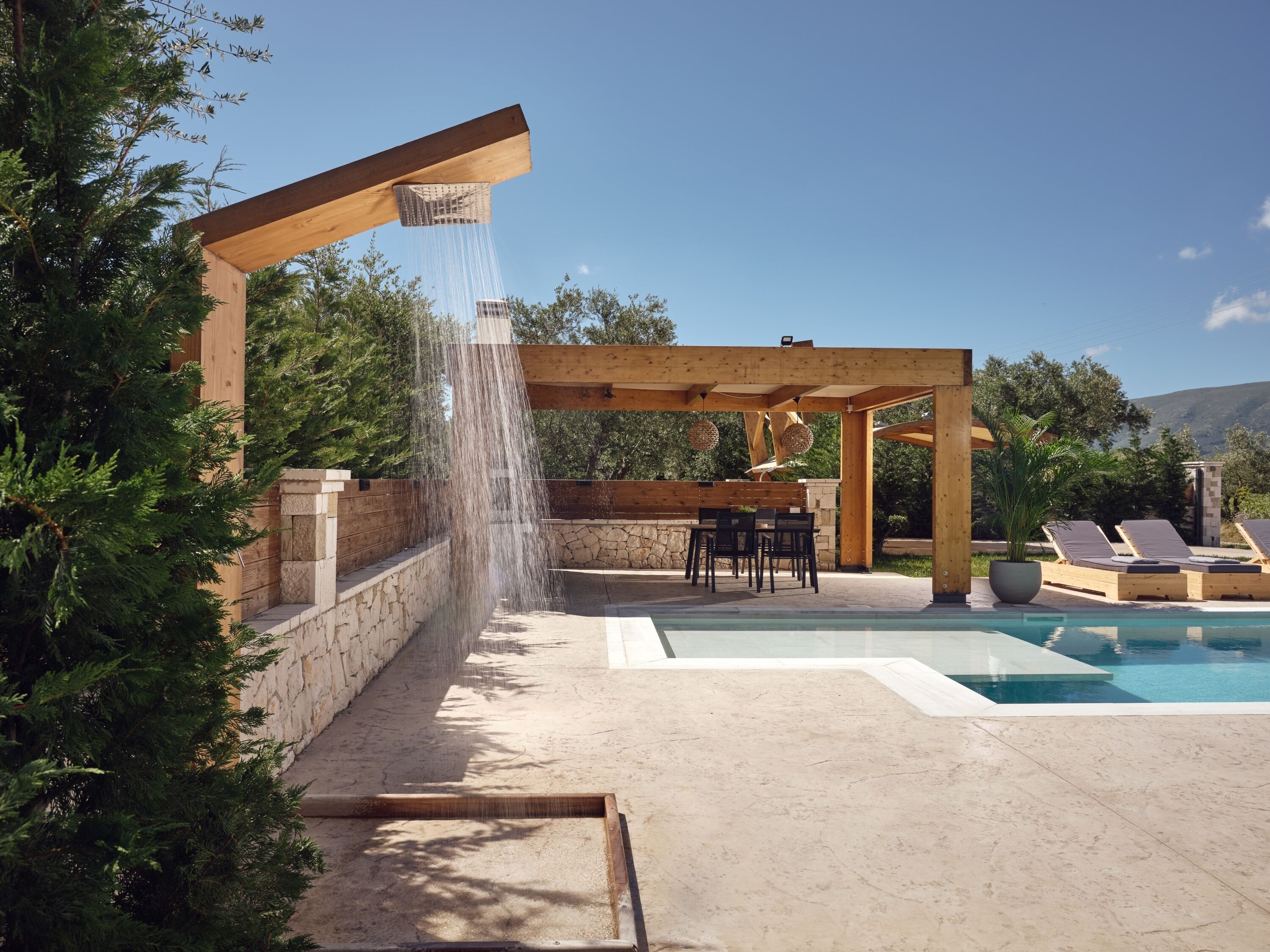 Eine hölzerne Pergola mit Wasserspiel, Sitzgelegenheiten im Freien und einem Pool.