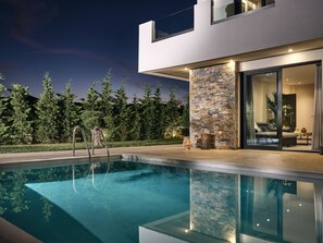 Ett modernt hus med en swimmingpool, en stenmur och glasdörrar som leder in till ett vardagsrum.