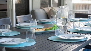 Una mesa de comedor dispuesta con platos, cubiertos y vasos, con una jarrón de agua y un tazón de uvas.
