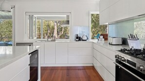 Una cocina moderna con armarios blancos, lavavajillas integrado, estufa a gas y un amplio ventanal con vistas a árboles.