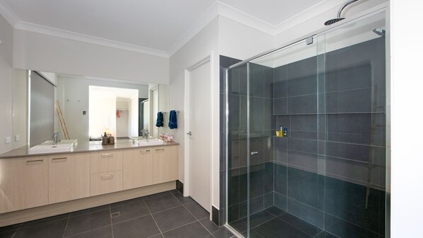 A modern bathroom with a glass-enclosed shower, a large mirror, and a vanity with a sink and towel rack. - Surf and Dunes - Beachside Living with a Heated Pool & Pet-Friendly (Yamba)
