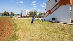 Área residencial com um edifício branco, um parquinho infantil com escorregadores e um banco.