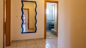 Um corredor com chão ladrilhado, um espelho com moldura azul e uma porta que dá para um banheiro.