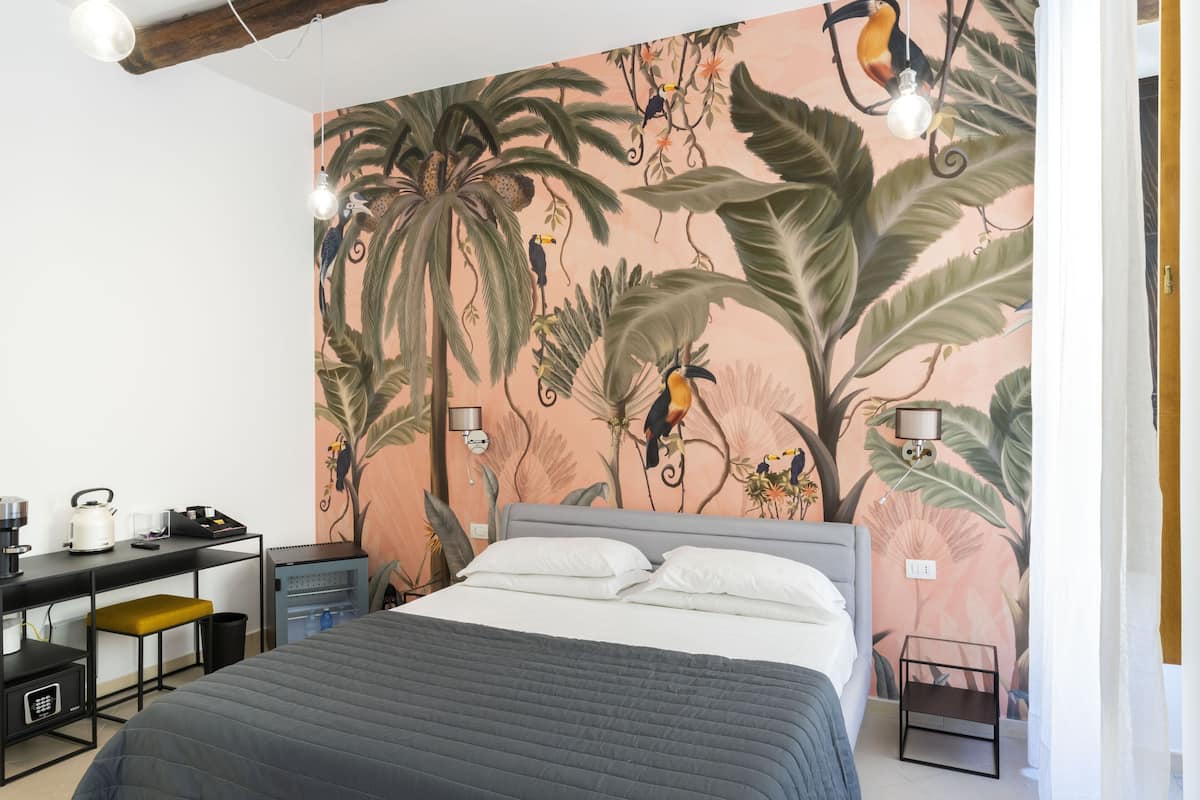 Een slaapkamer met een bed, een bureau en een stoel. Op de muur is een muurschildering met vogels en planten.