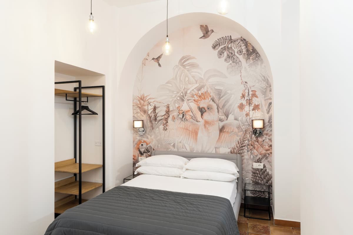 Een slaapkamer met een bed, een houten wandplank en een muurschildering van vogels en begroeiing.