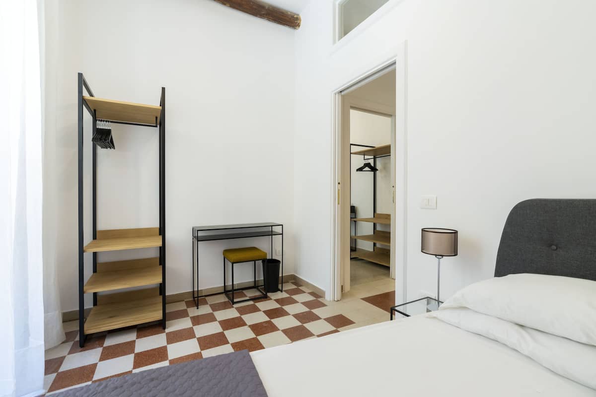 Een slaapkamer met een bed, een bureau, een stoel, een wandplank en een inloopkast.