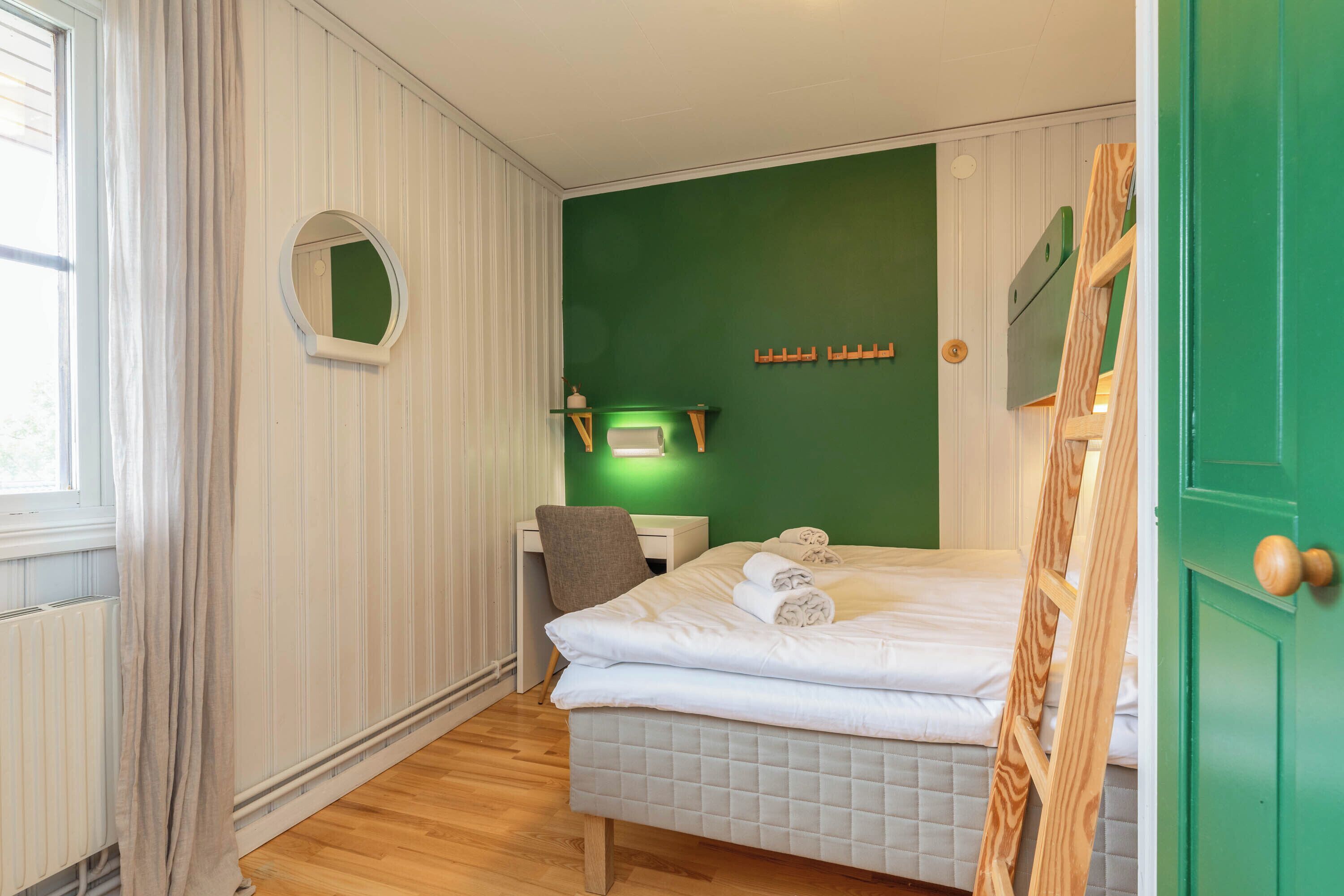 Una camera d'albergo con un letto, una scrivania, una sedia, uno specchio e una parete verde.