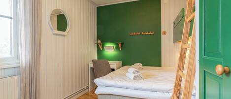 Una camera d'albergo con un letto, una scrivania, una sedia, uno specchio e una parete verde.