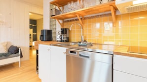 A modern kitchen with a dishwasher, coffee maker, and a wooden shelf with cups and glasses.