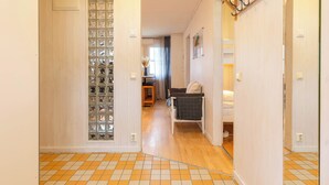 A hallway with a tiled floor, a wooden door with a glass block panel, and a coat rack.