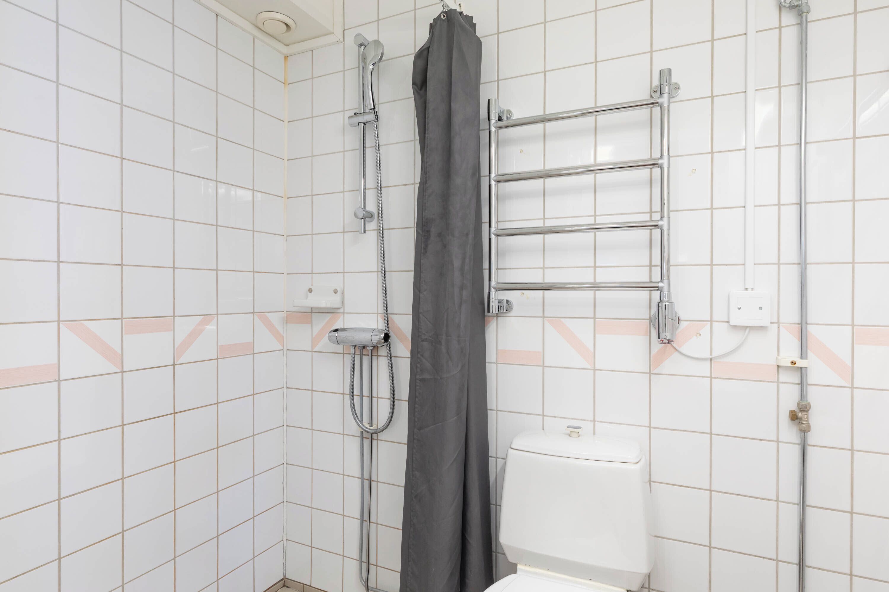 A bathroom with white tiled walls, a shower with a grey curtain, a white toilet, and a towel rack.