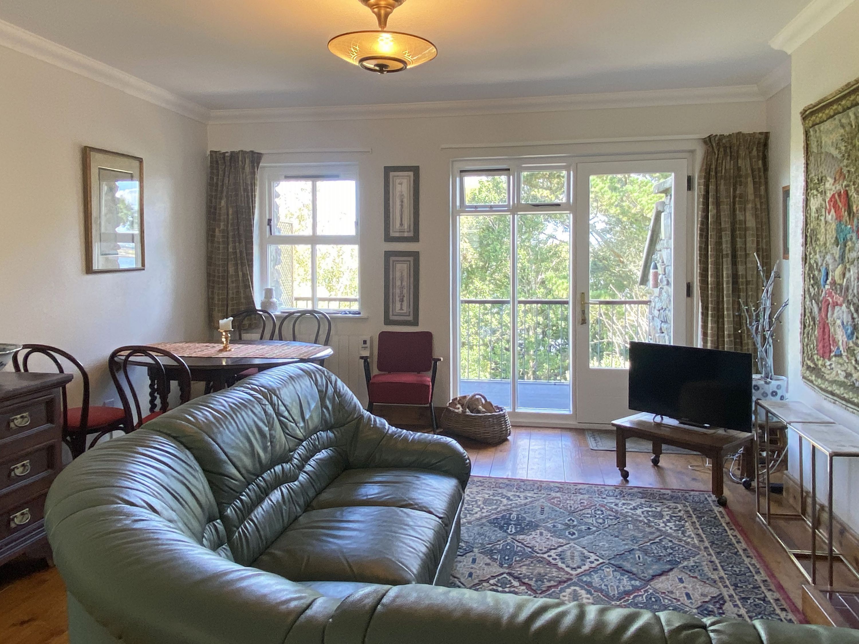 A living room with a leather sofa, a dining table with chairs, a television, and a large window with curtains.