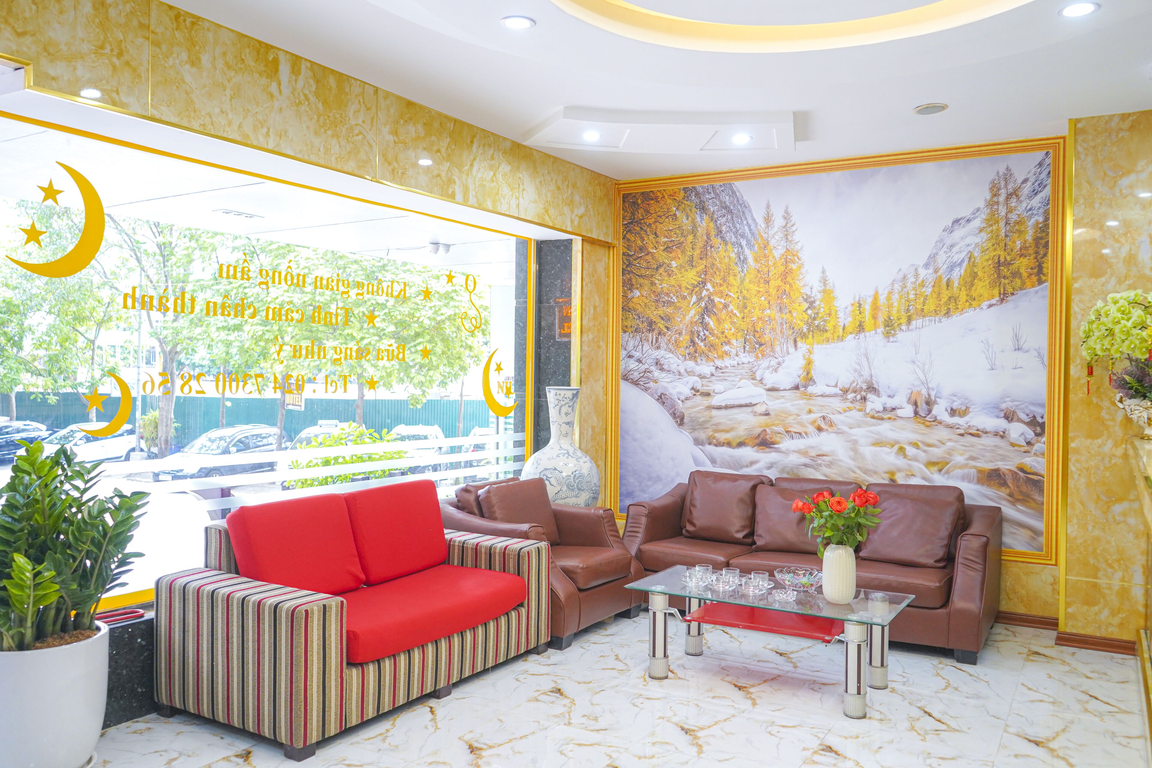 A lobby with a red sofa, a brown sofa, and a striped sofa. There is a vase with flowers on a table.