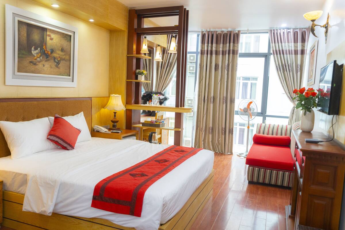 A hotel room with a large bed, a desk, a chair, a TV, and a window with curtains.