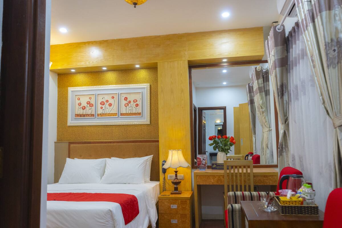 A hotel room with a bed, bedside table, lamp, chair, and a desk with a mirror.