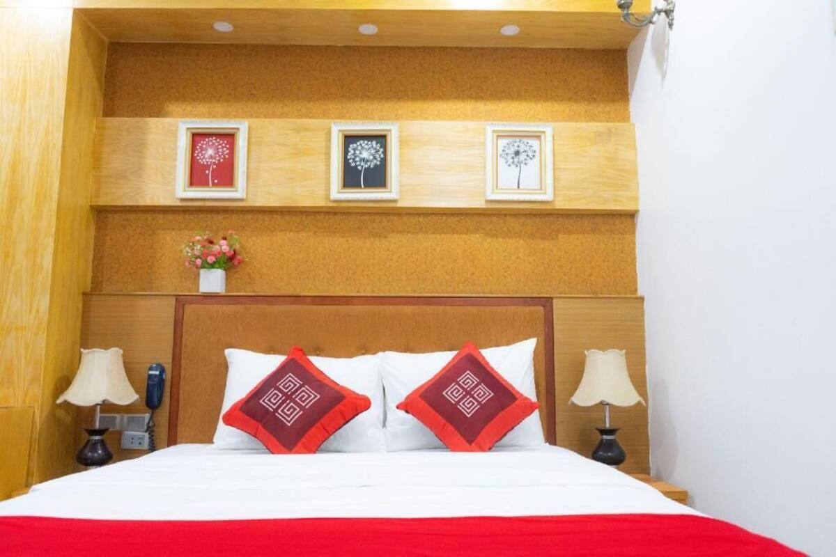 A hotel room with a wooden headboard, a bed with white and red bedding, two bedside lamps, and three framed pictures on the wall.