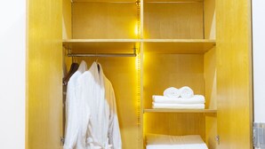 Un armario de madera con varios estantes, una barra para colgar ropa y un asiento plegable.