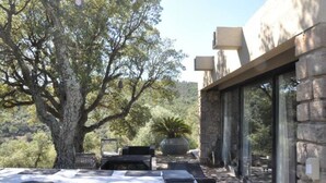 An outdoor dining area with stone walls, a large tree, and a view of the surrounding landscape.