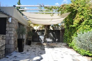 En innergård med stenplattor, en pergola med ett solskydd, utomhusmöbler och frodig grönska.