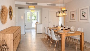 Un espace repas moderne avec une table en bois dressée pour six personnes, des chaises blanches et un lustre.