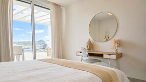 Une chambre d’hôtel avec un grand lit, un bureau avec une chaise, un miroir rond et une vue sur l’extérieur.