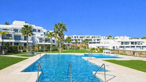 Une piscine à l’eau d’un bleu cristallin, entourée d’une pelouse bien entretenue et de palmiers.