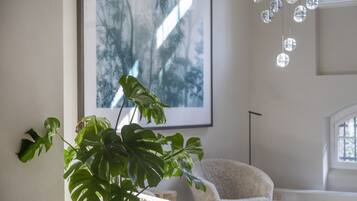 A room with a large plant, a framed artwork, a white chair, and a hanging light fixture.