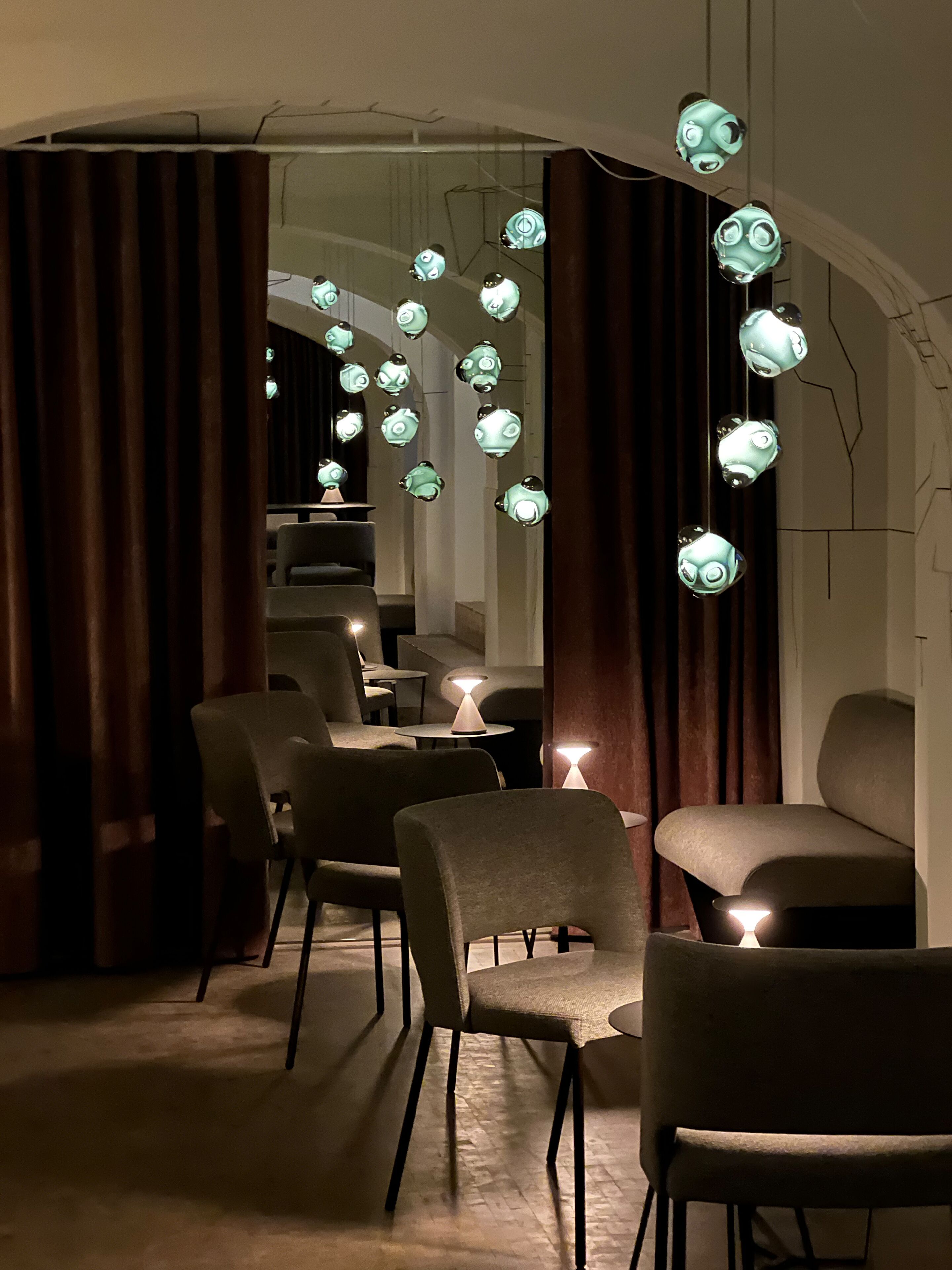 A modern interior with hanging spherical lights, dark curtains, and contemporary furniture.