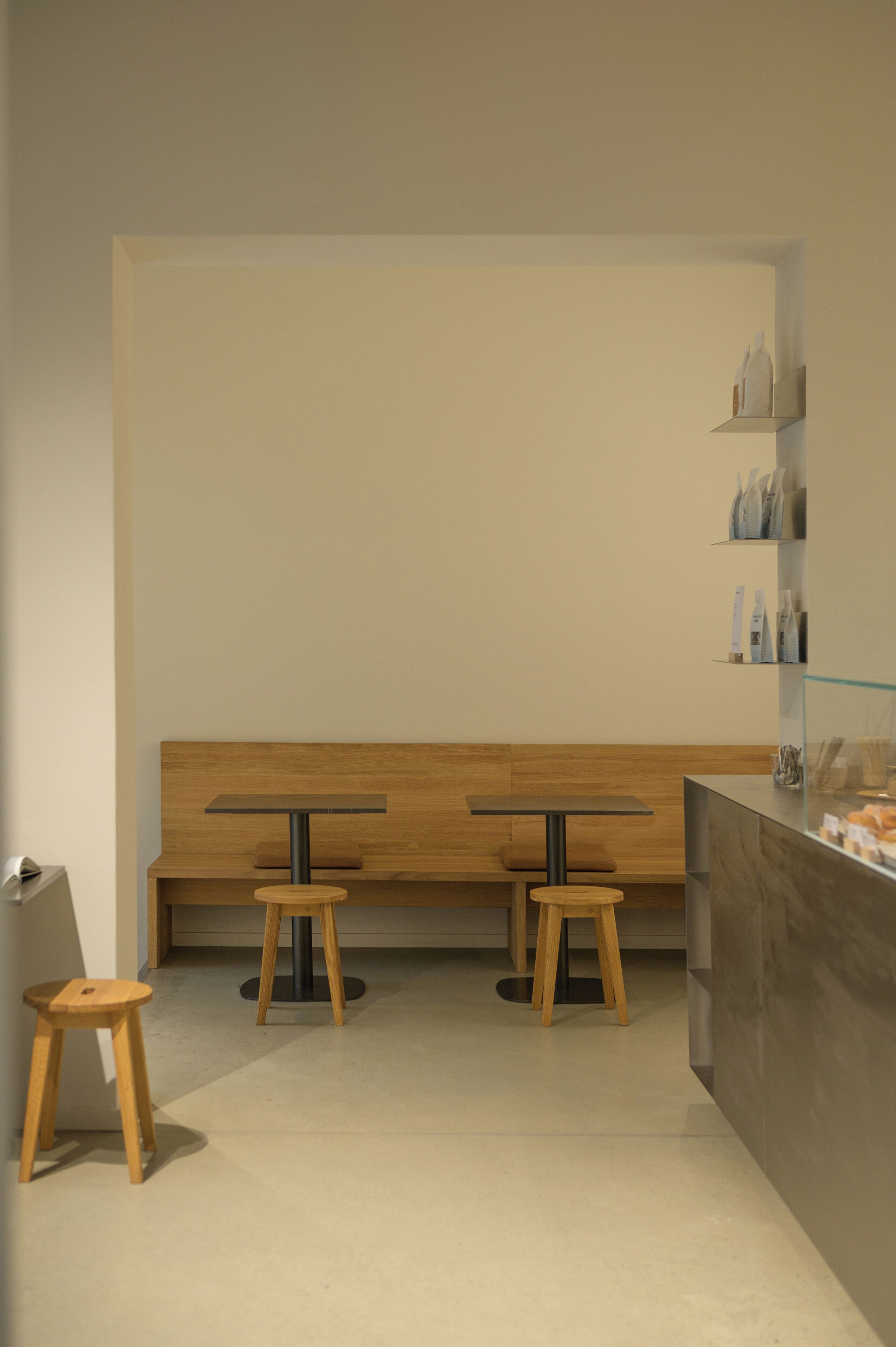 Un café moderne avec deux tables et des tabourets en bois, un banc et un comptoir doté d’une vitrine.
