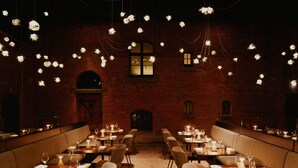 A restaurant with multiple tables and chairs, a brick wall, and hanging lights.