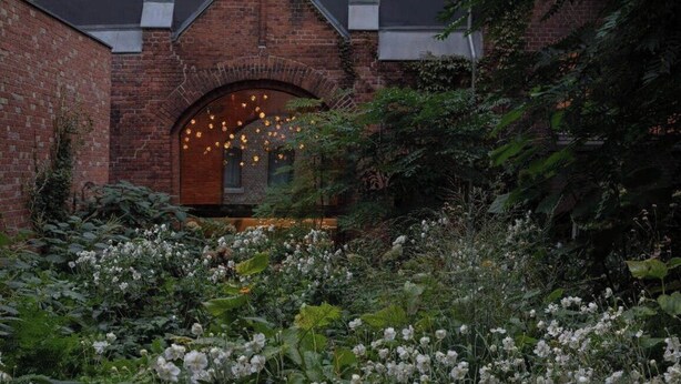 A brick building with an arched entrance and a garden with white flowers.