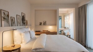 A hotel room with a large bed, a desk with a chair, a vanity with a mirror, and framed botanical prints on the wall.