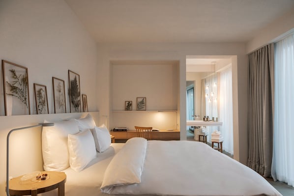 A hotel room with a large bed, a desk with a chair, a vanity with a mirror, and framed botanical prints on the wall. - Wilmina Hotel (Berlin)