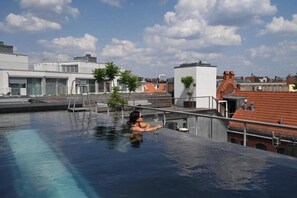 A rooftop swimming pool with a person relaxing, surrounded by modern buildings and clear skies. - Wilmina Hotel (Berlin)