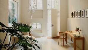 A spacious room with a high ceiling, large windows, and a wooden desk with chairs.