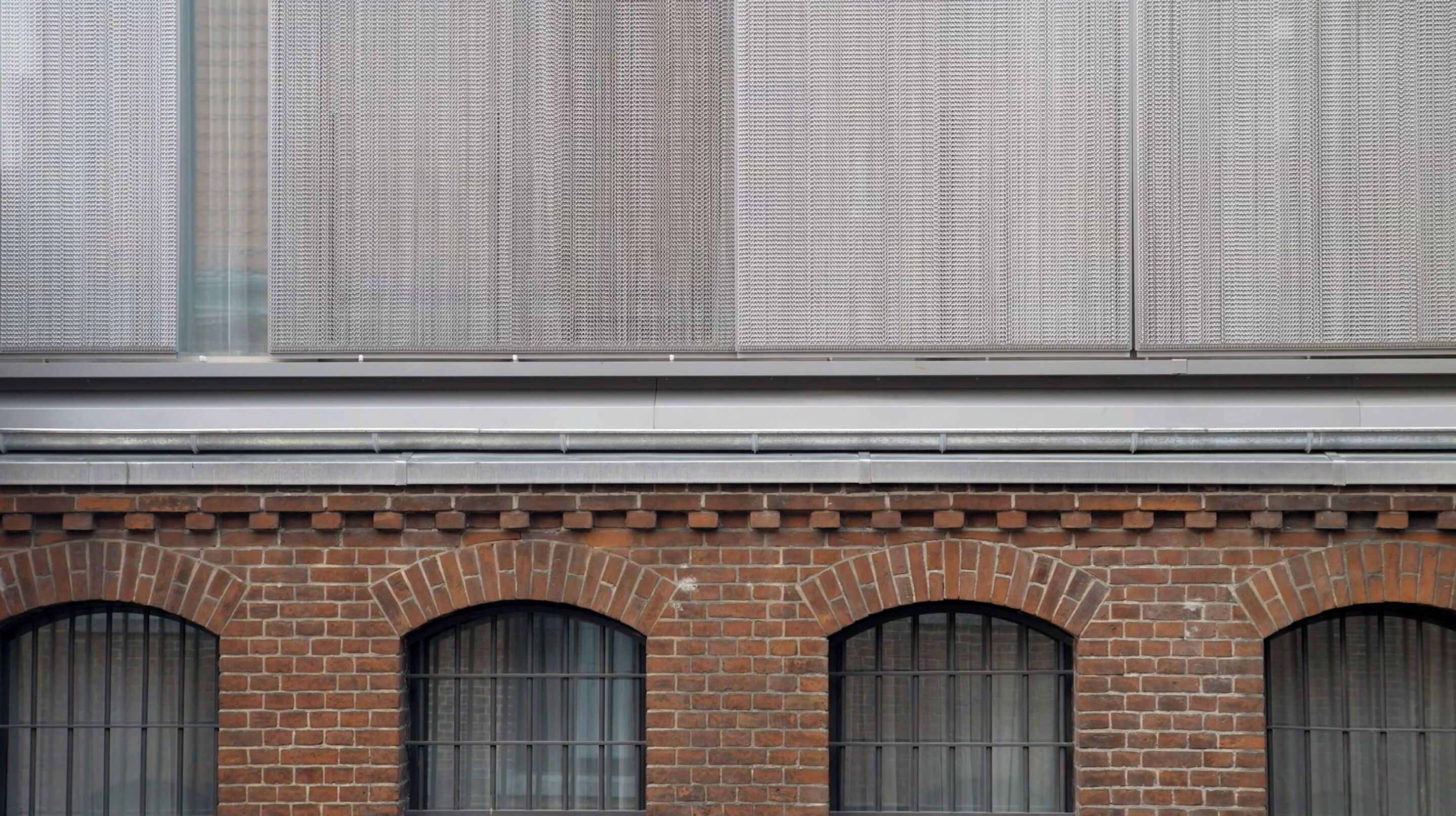 Fachada de edificio con una sección inferior de ladrillo y una sección superior de metal con líneas verticales.