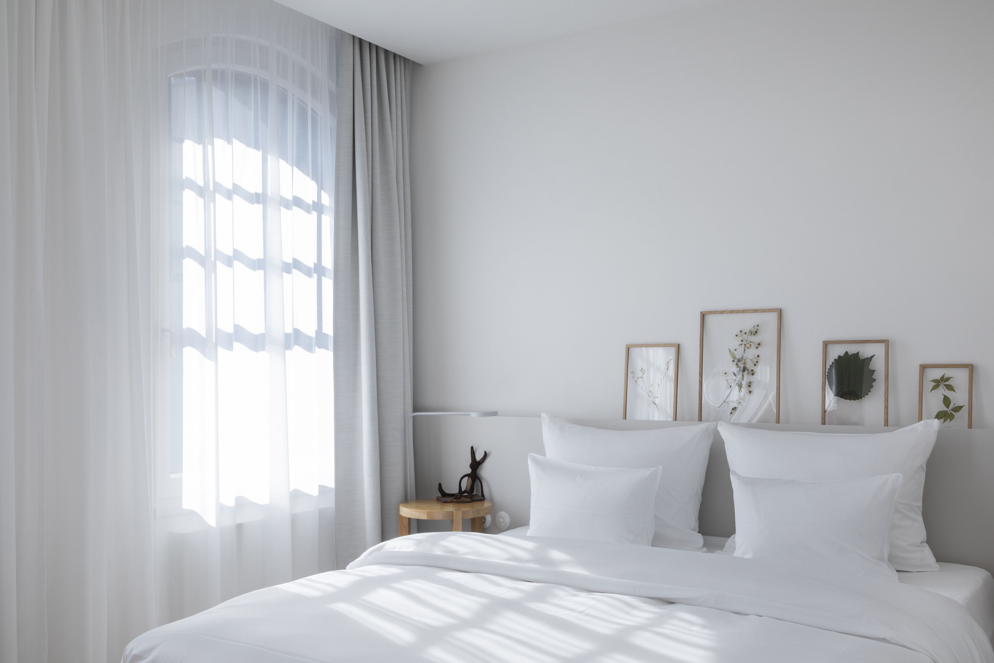 A bedroom with a bed, white curtains, a bedside table, and wall-mounted decor.