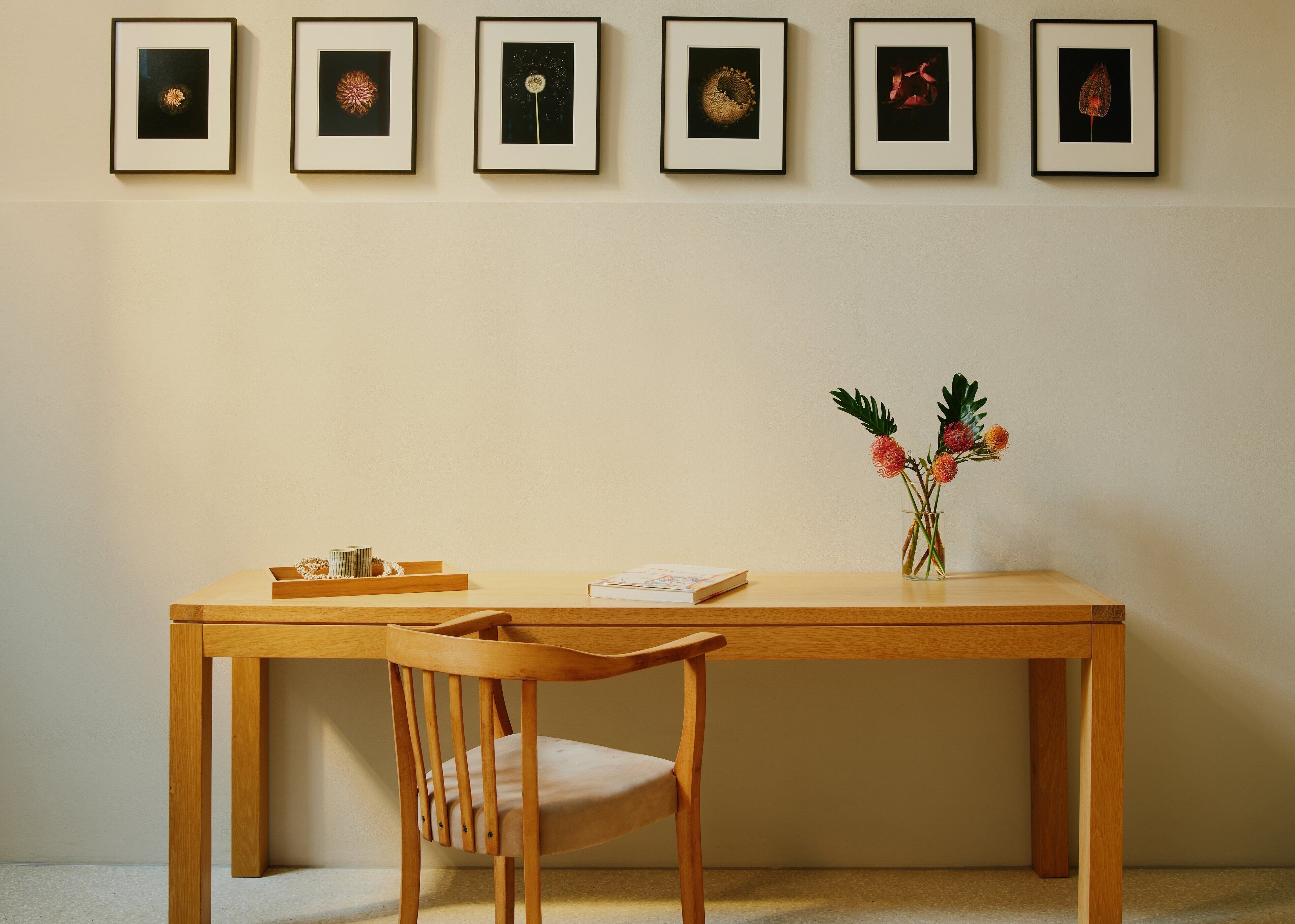Ein Holztisch mit Blumen in einer Vase, ein Stuhl und gerahmte Kunstwerke an der Wand.