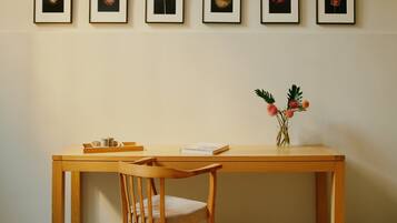 Ein Holztisch mit Blumen in einer Vase, ein Stuhl und gerahmte Kunstwerke an der Wand.