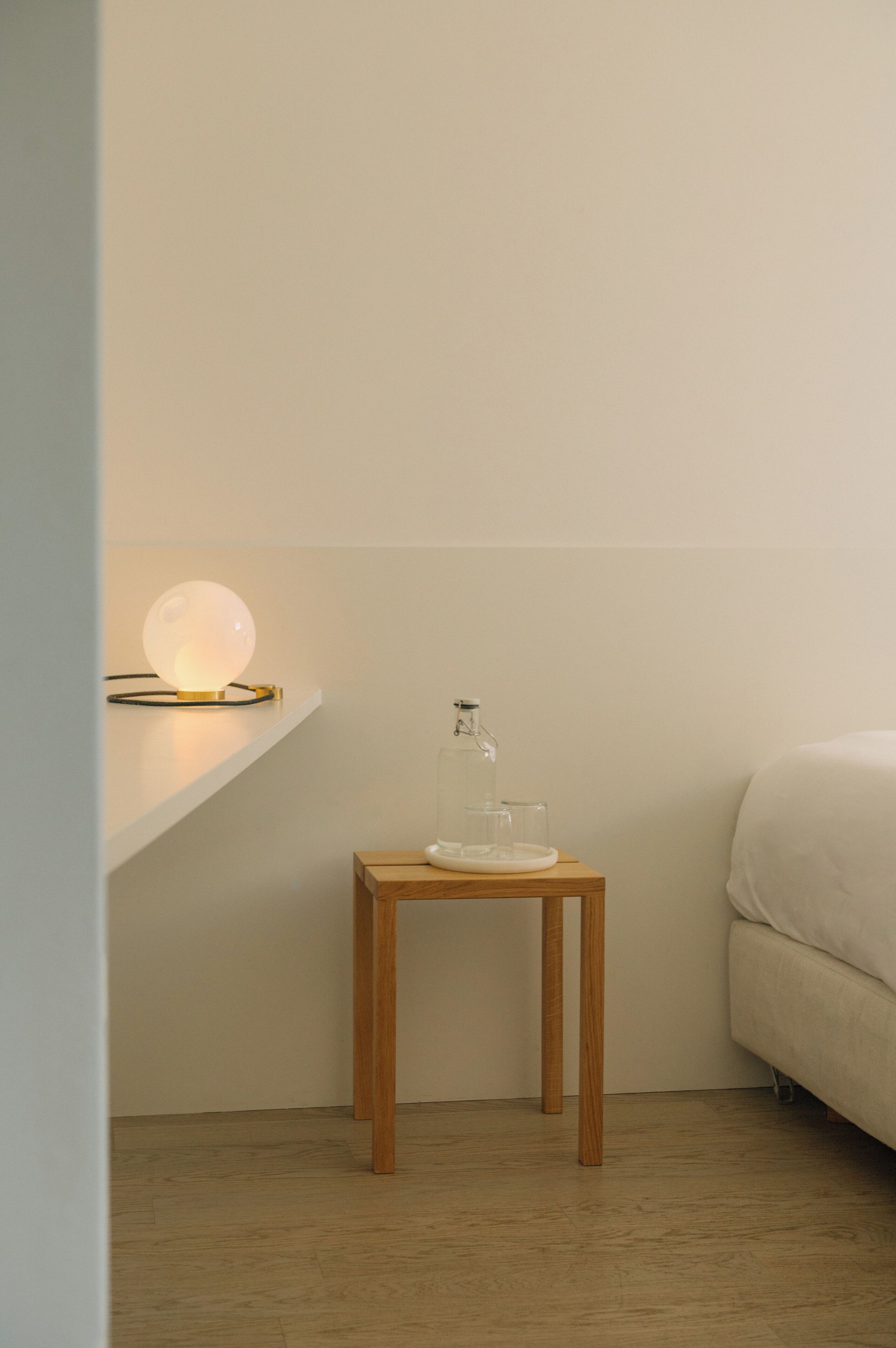 Une petite table de chevet en bois, avec une bouteille en verre et une lampe.