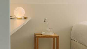 Une petite table de chevet en bois, avec une bouteille en verre et une lampe.