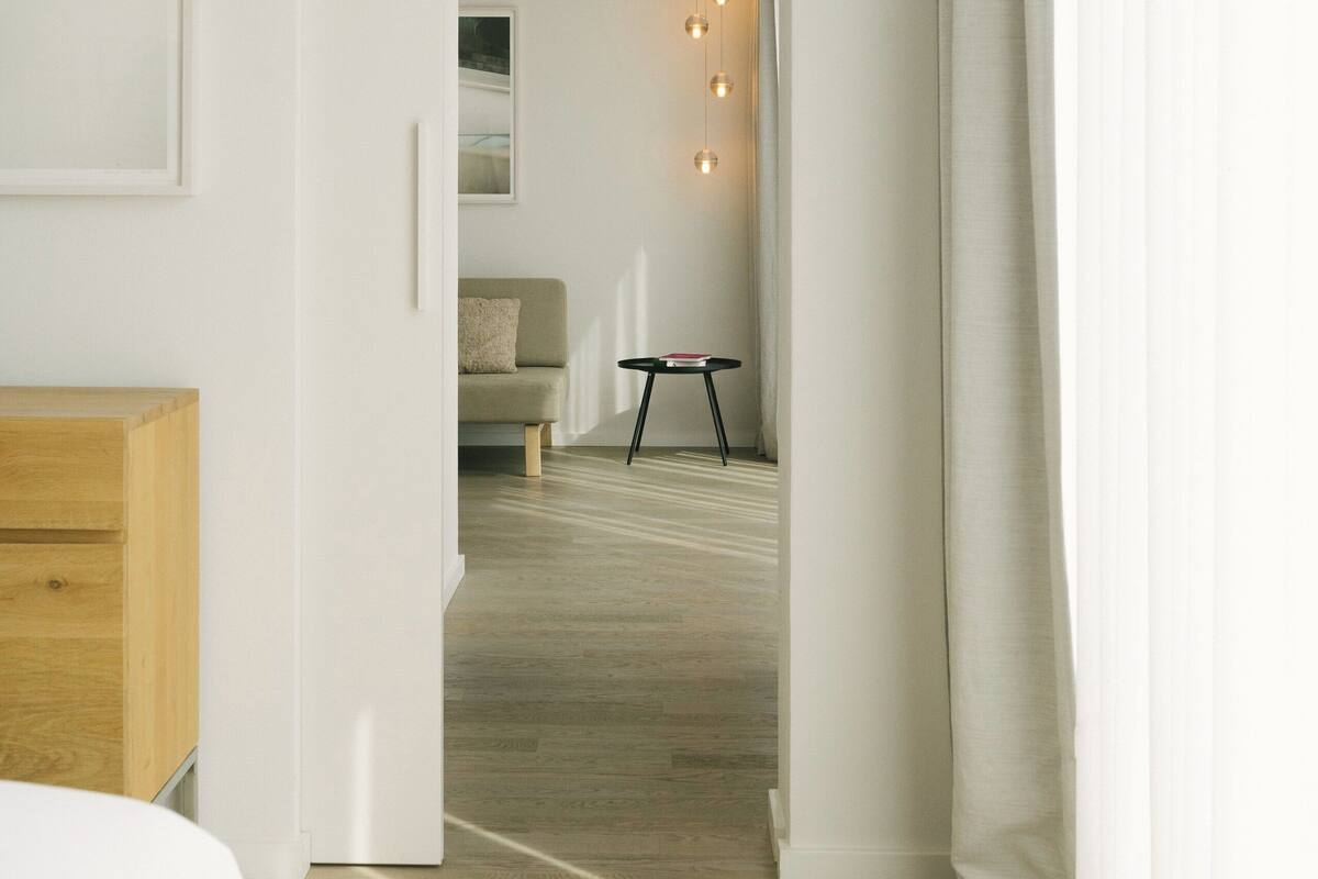 A modern interior with a wooden cabinet, a white door leading to a living area with a sofa, a small table, and hanging lights.