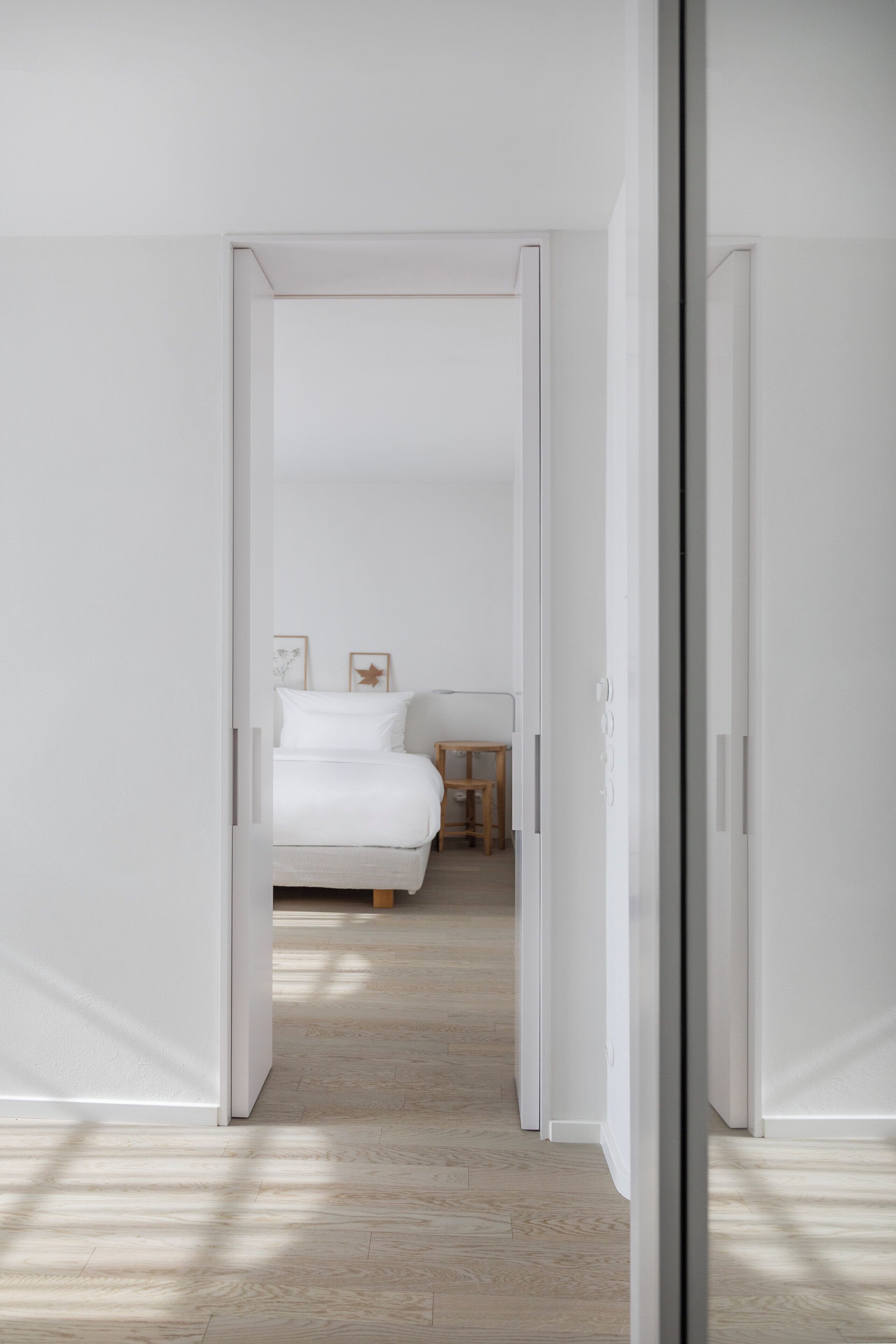 A narrow hallway leading to a bedroom with a bed, a small table, and framed pictures on the wall.