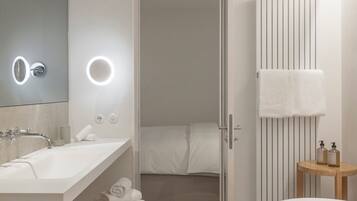 A modern bathroom with a large mirror, two sinks, a toilet, and a shower area.