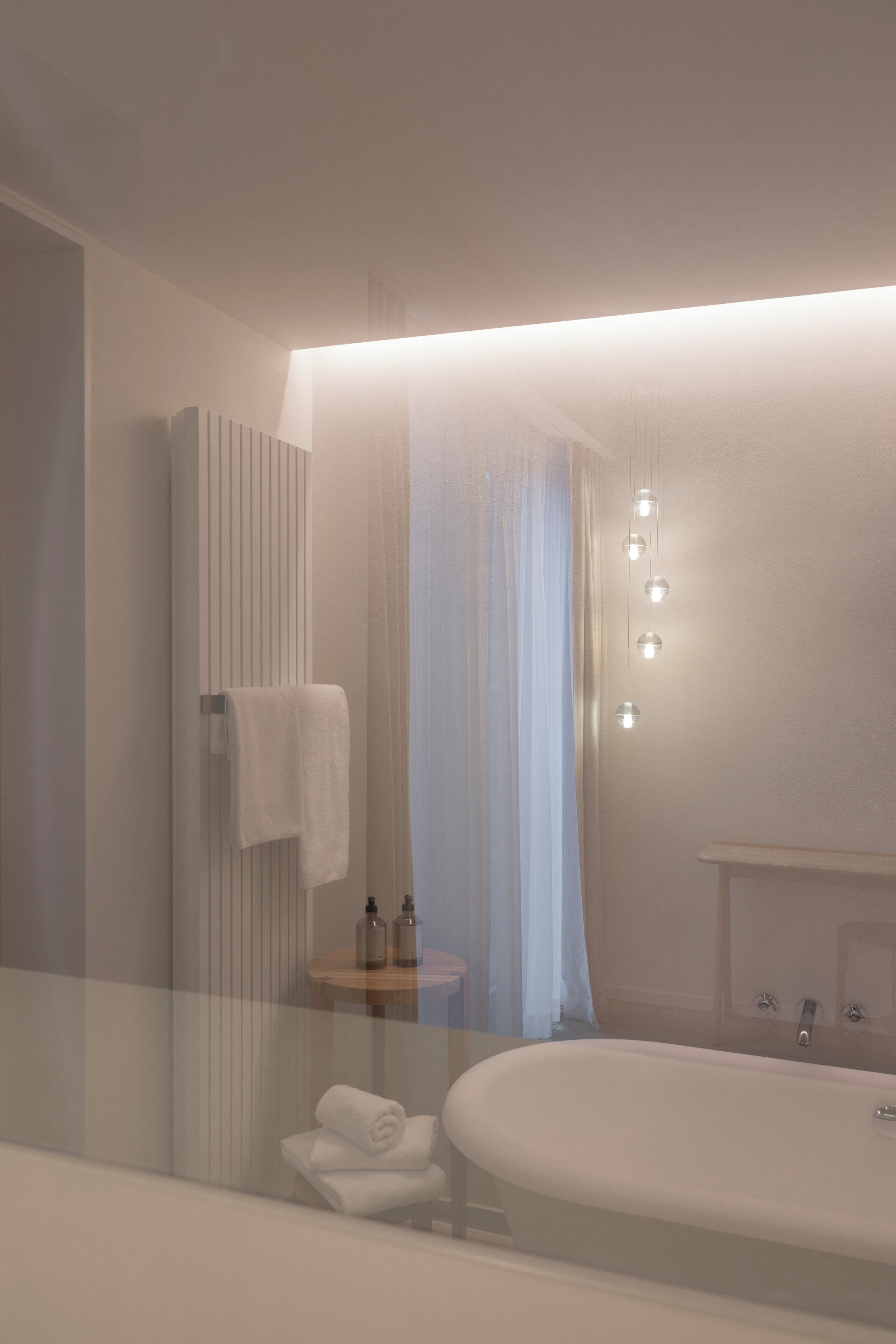 Un baño moderno con una bañera, un perchero para toallas, una mesita con botes y un espejo.