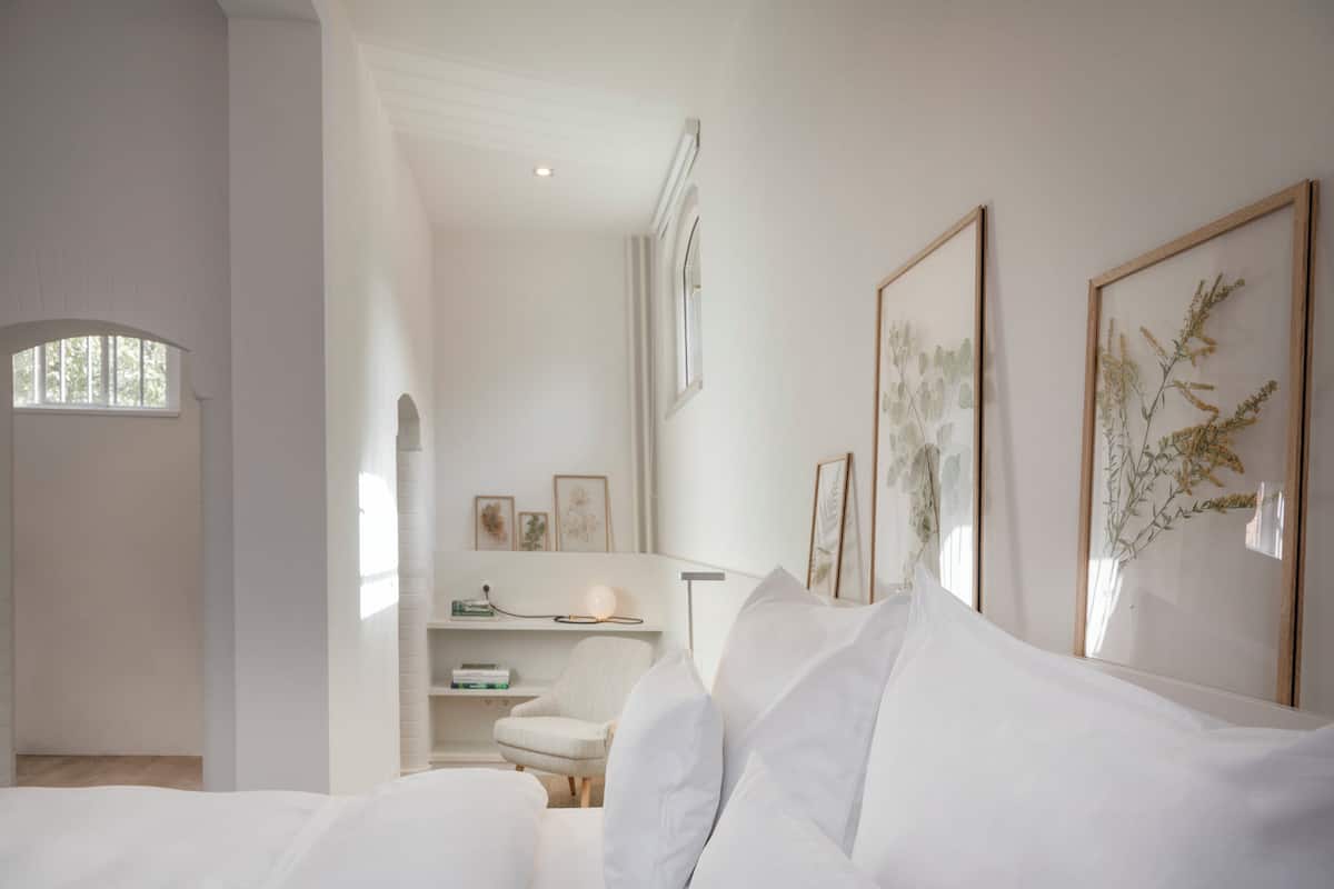 A minimalist bedroom with a bed, a chair, and framed botanical prints on the wall.